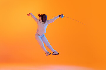 Studio shot of professional fencer in white fencing costume and mask in action, motion isolated on orange color background. Sport, youth, activity, skills,