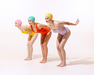 Portrait of three young women in vintage retro swimming suits posing isolated over grey studio background
