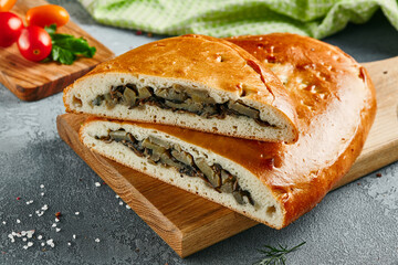 Mushroom pie on wooden board with ingredients. Composition with mushroom pie on concrete background with textile and spices. Homemade pie with potato and mushroom in rustic style on gray table.