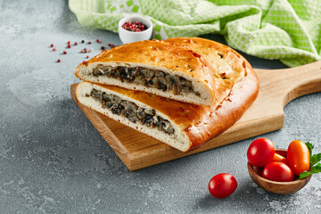 Classic pie with mushroom on wooden board. Composition with mushroom pie on concrete background with textile and spices. Homemade pie with mushrooms and onion in rustic style on gray table.