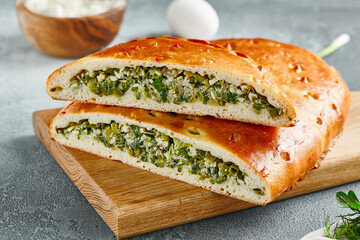 Classic pie with green onion and egg on wooden board. Composition with egg and onion pie on concrete background with textile and spices. Homemade pie with onion and egg in rustic style on gray table.