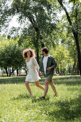 Naklejka na ściany i meble full length of cheerful young couple having date while walking in green park.