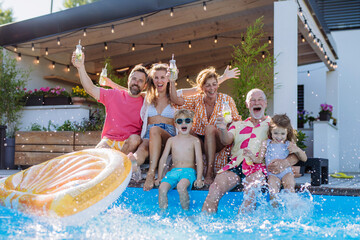 Multi generation family enjoying drinks and splashing when sitting at backyard pool.