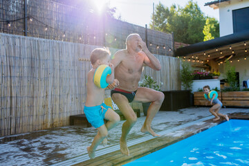 Grandfather with his granson having fun together when jumping into the swimming pool at backyard.
