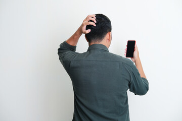 Back view of a man scratching his head while looking to his handphone