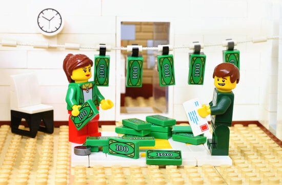 L&ouml;rrach, Germany - July 11h 2022: Lego minifigures in office or bank are washing the money cash. Editorial illustrative image of business occupation or crime.