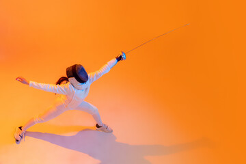 Aerial view of professional fencer in white fencing costume and mask in action, motion isolated on orange color background. Sport, youth, activity, skills,