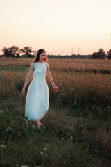 Fototapeta na wymiar A beautiful pretty girl is dancing on a field at sunset in a white dress. Happy woman. Concept. Bride