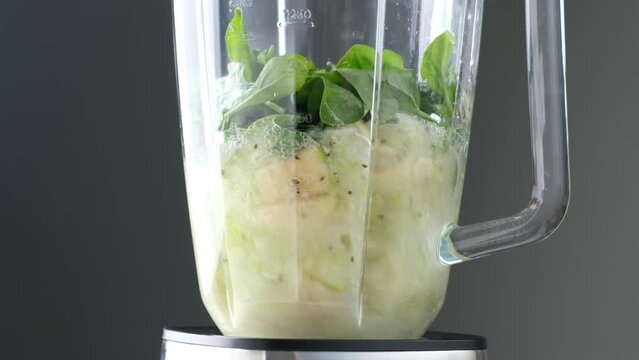 Fruits and spinach mixing in blender cup in slow motion. Cooking process of healthy vegan smoothie, superfood