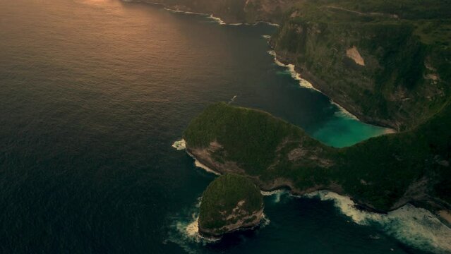 Bird's eye view of Nusa Peneda island covered with greenery against the blue sea in Bali at sunset