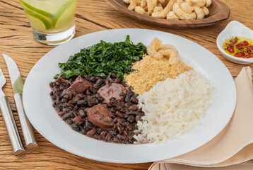 Typical brazilian feijoada with rice, pepper, farofa, kale, caipirinha and cracklings