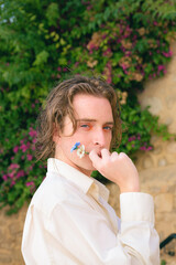 Fototapeta premium Attractive young man with make-up poses with flowers looking at camera