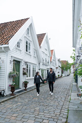 Young couple walking along a street in Stavanger with typical Scandinavian white houses in Norway.