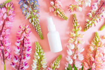 White cosmetic spray bottle and pink lupine flowers on pink background. Front top view, summer flat lay, mockup, template.