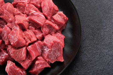 Raw chopped beef meat. Raw organic meat beef or lamb, spices, herbs on black plate on dark grey concrete background. Goulash. Raw uncooked meat. Meat with blood. Top view with copy space.