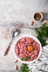 Raw minced meat. Ground meat beef, pork or lamb spices, herbs and eggs on white plate on light grey concrete background. Fresh minced meat ready for cooking. Food cooking background. Top view.