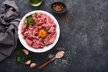 Raw minced meat. Ground meat beef, pork or lamb spices, herbs and eggs on white plate on black old concrete background. Fresh minced meat ready for cooking. Food cooking background. Top view.