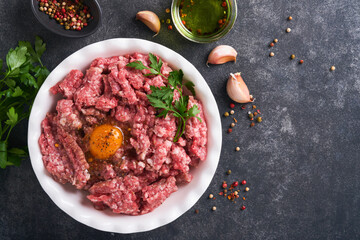 Raw minced meat. Ground meat beef, pork or lamb spices, herbs and eggs on white plate on black old concrete background. Fresh minced meat ready for cooking. Food cooking background. Top view.