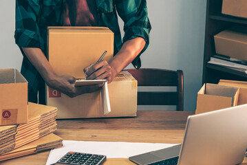 Young entrepreneur business owner work at home, small business startup receive order client and take note working with report and pack the product on purchase delivery online to sending destination.