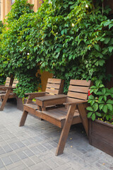 Fototapeta na wymiar Wood bench in the bushes. Wood chairs with table in front of cafe.