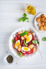 Tuscan Panzanella salad. Fresh tomatoes salad with basil leaves, eggs, olive oil and onion in white bowl on light background. Vegetarian panzanella salad. Mediterranean healthy food. Top view.