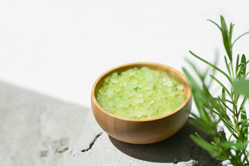 Wooden bowl with green bath sea salt with rosemary branch. Beauty treatment for spa and wellness on grey and white background. Skincare natural cosmetic concept for body care