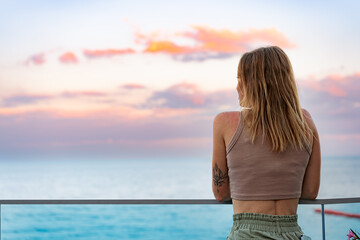 Obraz premium Beautiful young woman standing and looking at the sea and sky