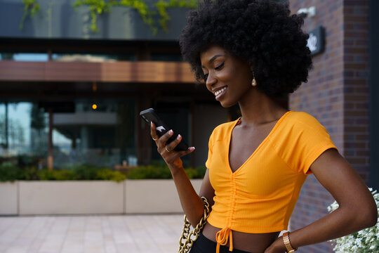 Smiling afro-american woman holding mobile phone while walking in the street