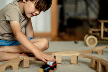 a boy at home in a room is building a railway, a child is playing with a toy train. Educational toys for home and kindergarten. Wooden Environmental Toys