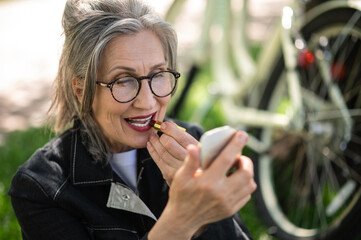 A mature woman in eyeglasses doing make up