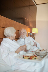 Fototapeta na wymiar A senior happy couple enjoying breakfast while staying in bed