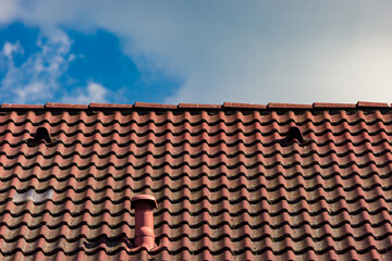 Naklejka premium Red roof tiles against cloudy sky with small chimney and ventilation holes