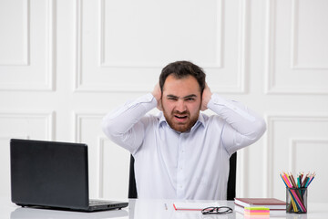 ADHD young brunette office worker at work behind the desk with the computer covering ears annoyed