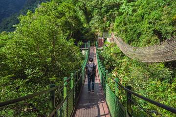 an adult man across the hills by using the suspension bridge with the another rope way on the right side.