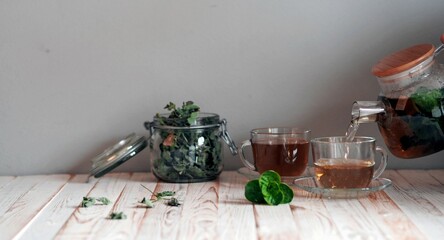 Cups with medicinal mint tea with a bunch of fresh mint and a teapot on a gray background. Herbal tea.
