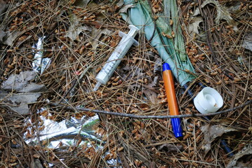 Trash littering the ground in the forest left behind by unscrupulous humans. The environmental impact of addiction, drug and alcohol use. - obrazy, fototapety, plakaty