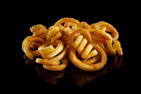 Heap of tasty golden fries potatoes with curly shape on surface isolated on black background