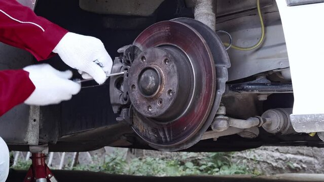 Brake system of a car, safety on the road. Close up car mechanic unscrews the brake pads, removing spring and caliper. 