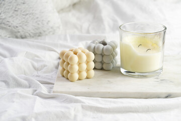 Three candles - bubble candles and white candle in glass jar with silver lid on marble tablet on...