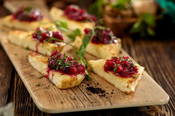 Hot appetizer for wine - grilled halloumi cheese with jam. Cheese appetizer baked halloumi on wooden background on rustic style. Adyghe cheese with berries dip on wooden table.