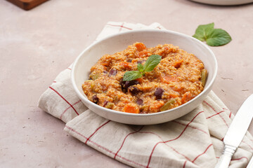 Grain dish - Millet with tomatoes, beans, carrots and spices, mint in a white bowl on a concrete round tray with checkered linen kitchen towel on purple background