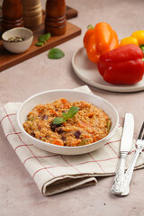 Grain dish - Millet with tomatoes, beans, carrots and spices, mint in a white bowl on a concrete round tray with checkered linen kitchen towel on purple background