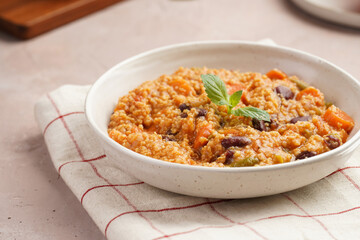 Grain dish - Millet with tomatoes, beans, carrots and spices, mint in a white bowl on a concrete round tray with checkered linen kitchen towel on purple background