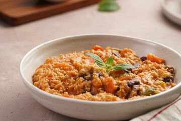 Grain dish - Millet with tomatoes, beans, carrots, bell pepper and spices, mint in a white bowl on a checkered linen kitchen towel on purple background