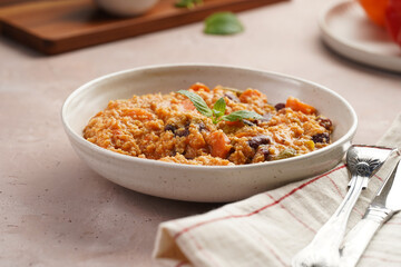 Grain dish - Millet with tomatoes, beans, carrots, bell pepper and spices, mint in a white bowl on a checkered linen kitchen towel on purple background