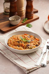Grain dish - Millet with tomatoes, beans, carrots, bell pepper and spices, mint in a white bowl on a checkered linen kitchen towel on purple background