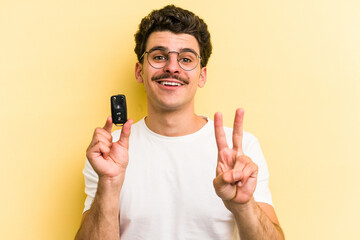 Young caucasian man holding car keys isolated on yellow background showing number two with fingers.