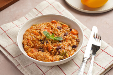 Grain dish - Millet with tomatoes, beans, carrots and spices, mint in a white bowl on a checkered linen kitchen towel on purple background