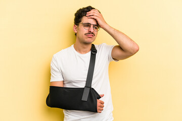 Young caucasian man with broke hand isolated on yellow background being shocked, she has remembered important meeting.