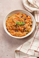 Grain dish - Millet with tomatoes, beans, carrots and spices, mint in a white bowl with checkered linen kitchen towel on purple background
